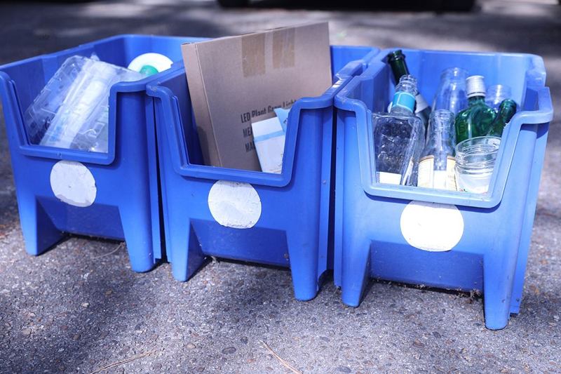 Cajas azules con cartón, botellas de plástico y vidrio, separados por material