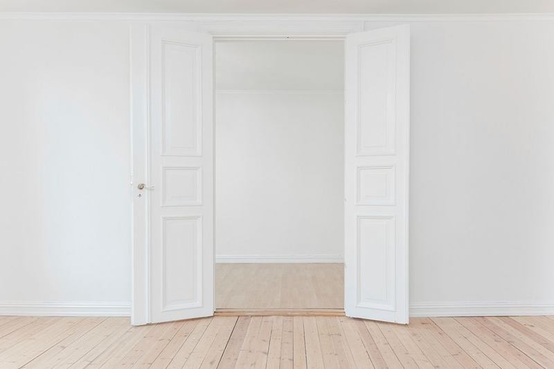 Puerta blanca de dos hojas abierta a una habitación vacía con suelo claro