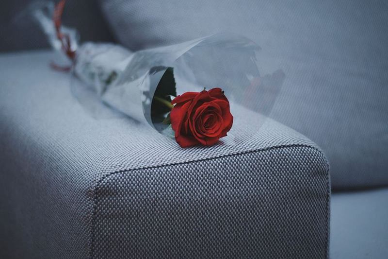 Sofá gris tapizado en tela fina con una rosa sobre el reposabrazos