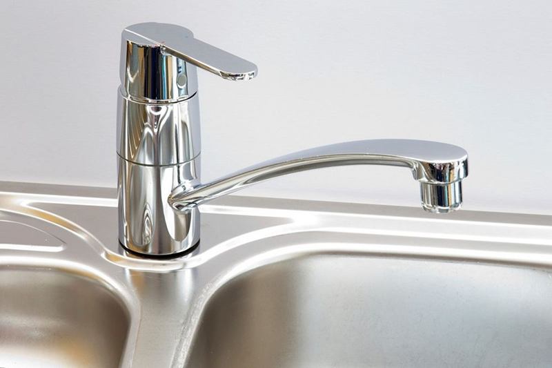 Shiny chrome mixer tap on a stainless steel sink, removing limescale from the tap