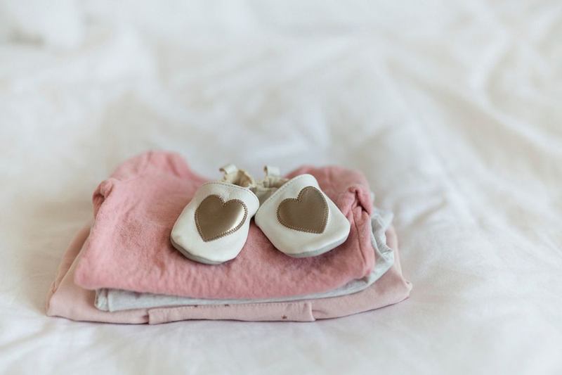 Ropa de bebé rosa recién lavada y zapatitos sobre una cama blanca