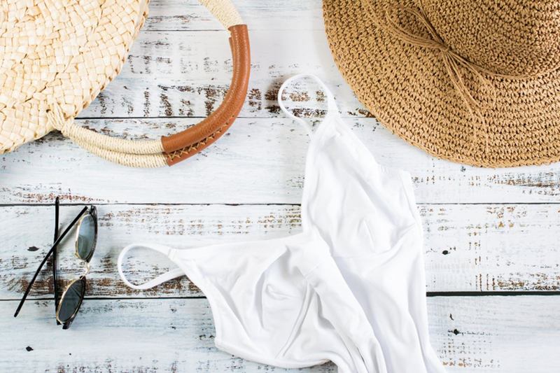 Bañador blanco extendido en plano sobre tablas claras junto a sombrero y gafas