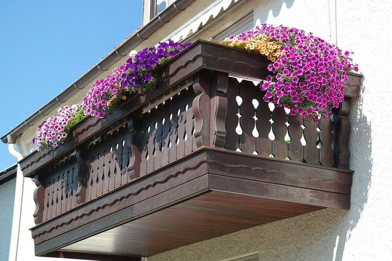 Wooden balcony with flowering window boxes on a white facade