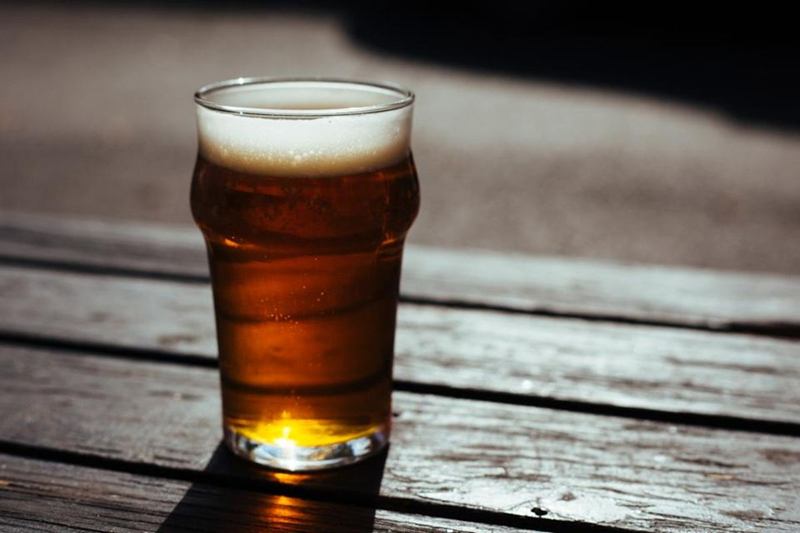 Vaso de cerveza lleno en una mesa de madera exterior, fuente de manchas pegajosas