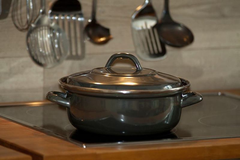 Cooking pot on a shiny ceramic hob with kitchen utensils behind