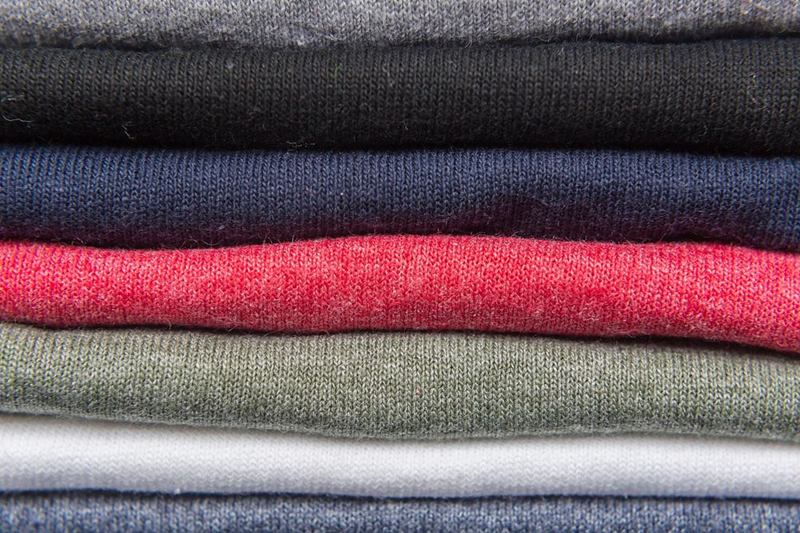 Pila de camisetas oscuras y de color, donde las manchas de lejía se notan