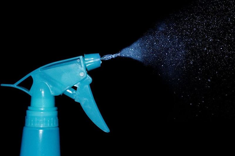 Pulverizador azul que suelta una fina nube de gotas sobre fondo oscuro