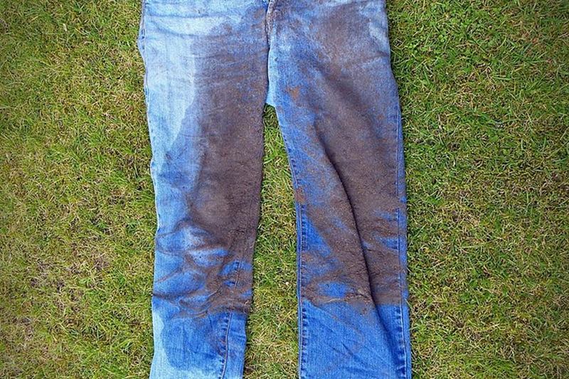 Vaqueros azules con grandes manchas de tierra extendidos en la hierba