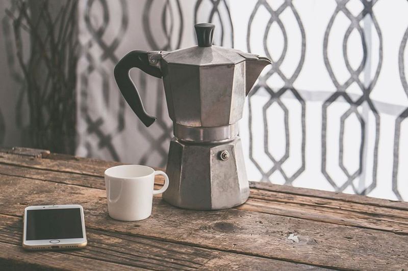 Cafetera italiana de aluminio y taza sobre una mesa de madera