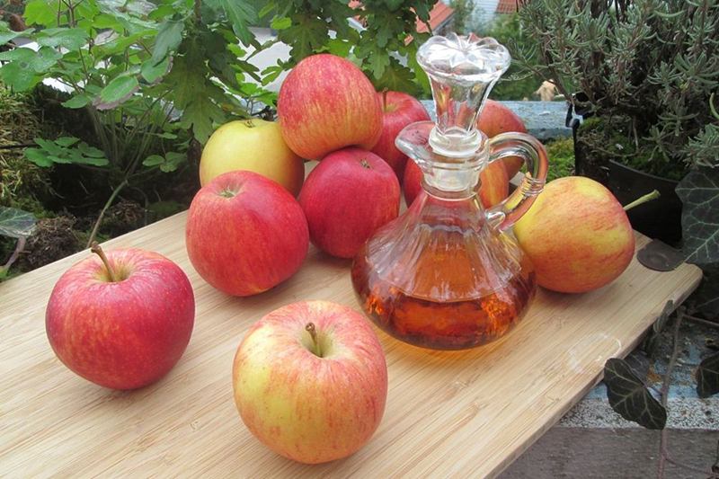 Aceitera de vidrio con vinagre de manzana junto a manzanas rojas en una tabla