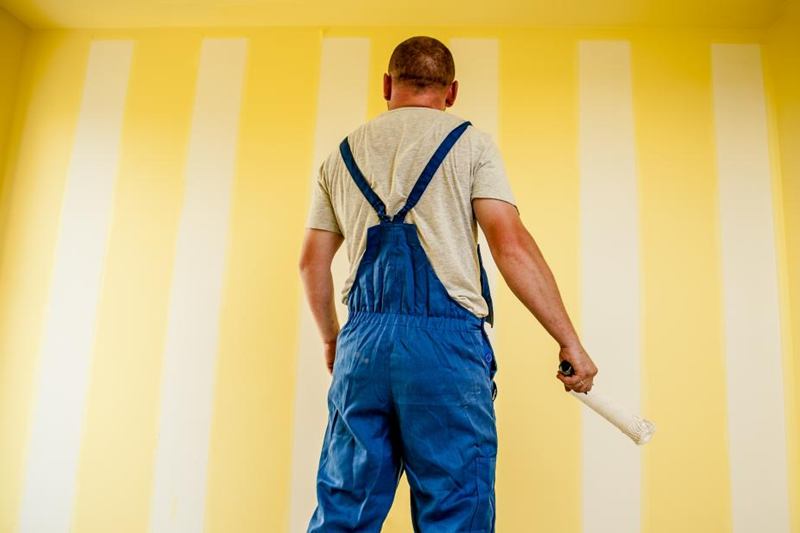 Pintor con rodillo ante una pared amarilla recién pintada, origen del olor a pintura