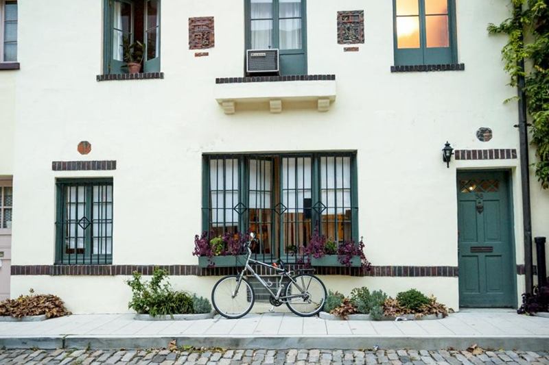 Fachada enlucida blanca con ventanas verdes, jardineras y una bici delante