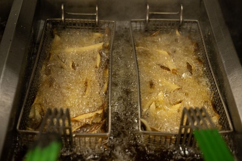 Patatas fritas en dos cestas sumergidas en aceite de freír de una freidora