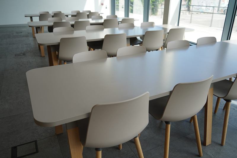 Sala común luminosa con mesas largas y sillas gris claro, ordenada tras la fiesta
