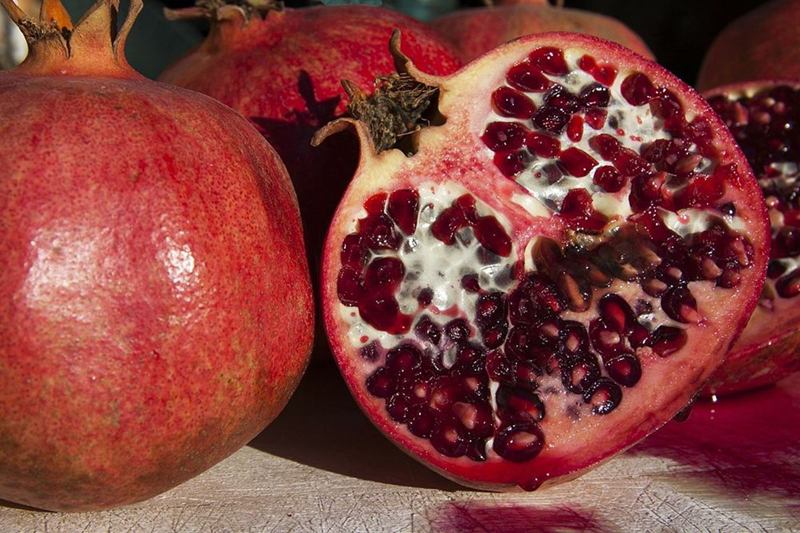 Granada abierta con granos rojos y manchas de zumo sobre la tabla de madera