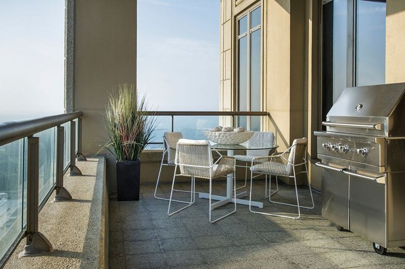 Balcón con sillas blancas, mesa de cristal, planta y barbacoa de gas cerrada