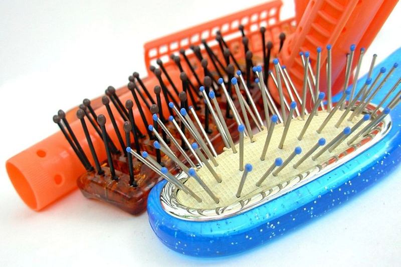 Cepillo azul de púas metálicas junto a otros cepillos y rulos