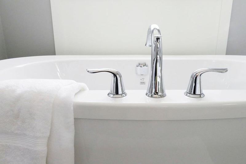 Bañera blanca con grifería cromada y toalla blanca en un baño luminoso