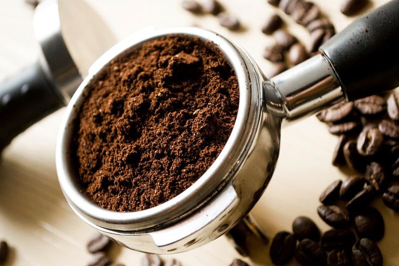 Portafiltro lleno de café molido entre granos, que acabará en posos de café