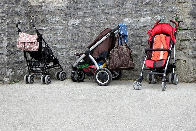 Tres carritos de bebé con bolsos aparcados junto a un muro de piedra