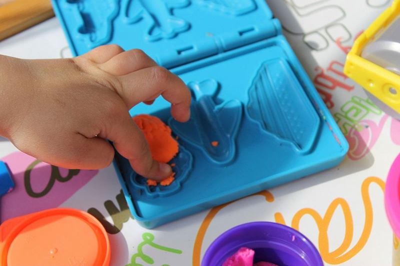 Mano infantil que presiona plastilina de colores en un molde
