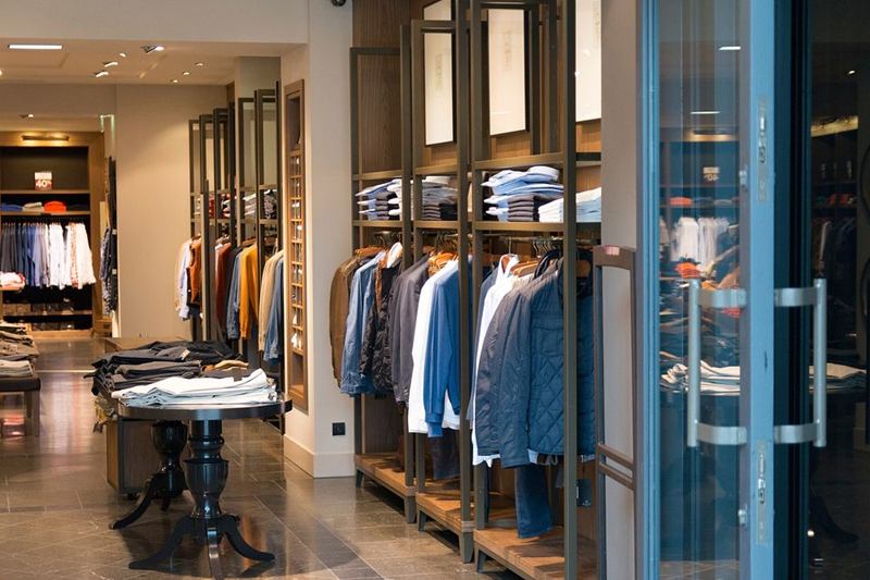 Tienda de ropa luminosa con puerta de cristal, estanterías y suelo reluciente