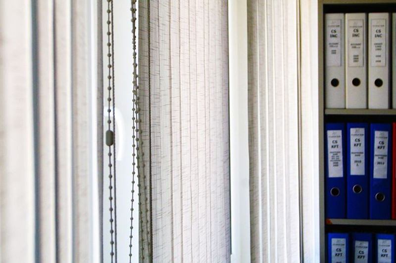 Cortina de lamas verticales blanca en una oficina junto a una estantería con archivadores