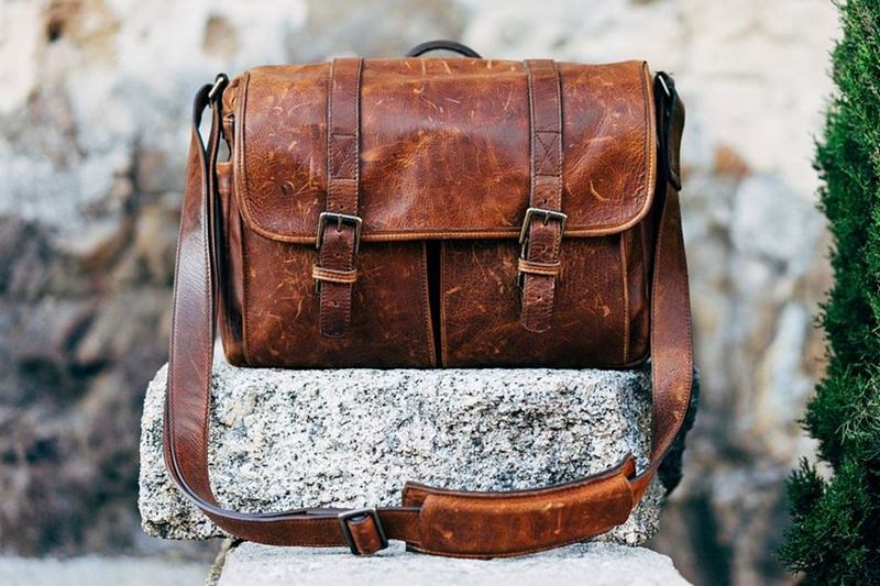 Bolso bandolera de piel marrón con hebillas apoyado sobre una piedra