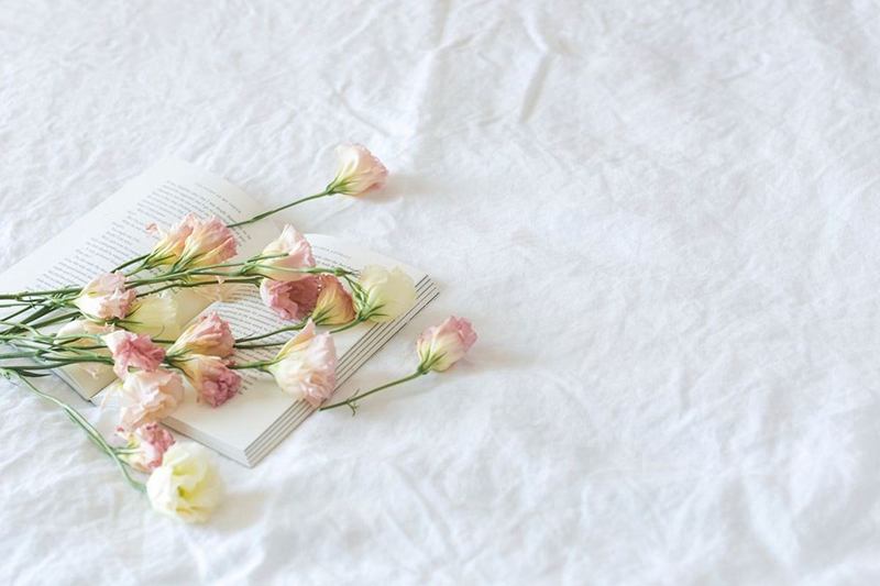 Ropa de cama de lino blanco con flores delicadas y un libro abierto