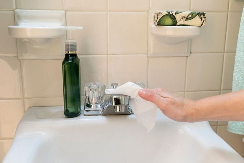 Mano que limpia el lavabo con una toallita desinfectante