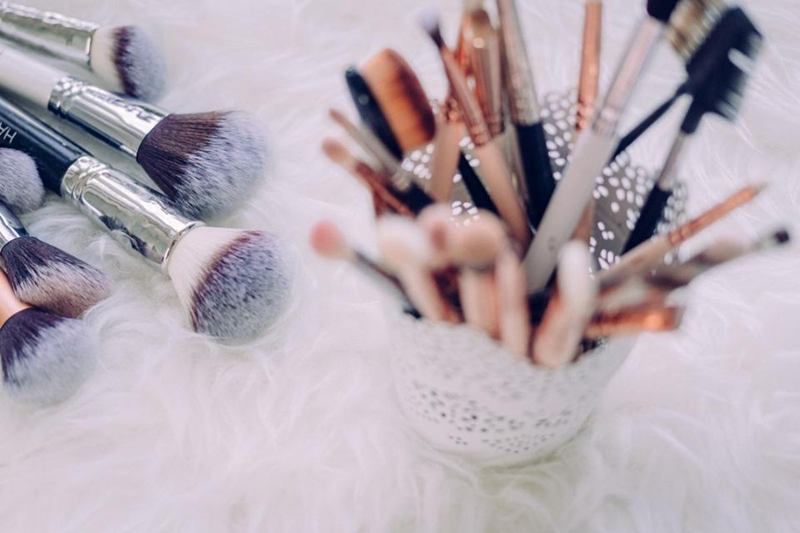 Brochas de maquillaje de varios tamaños en un vaso sobre una alfombra mullida