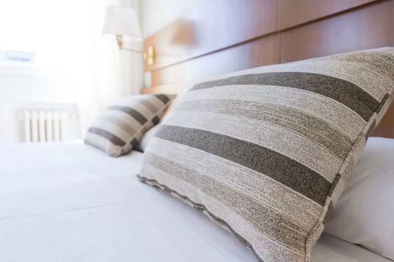 Cama blanca recién hecha con cojines a rayas en un dormitorio luminoso