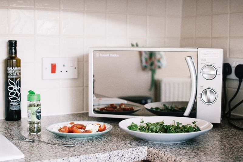 Microonde bianco sul piano cucina accanto a piatti con cibo