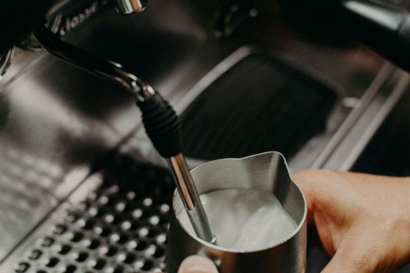Boquilla de vapor espumando leche en jarra de acero: limpiar el espumador de leche