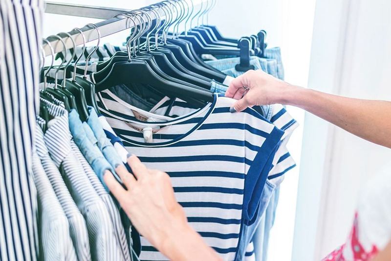Manos que eligen camisetas de rayas en un perchero de una tienda