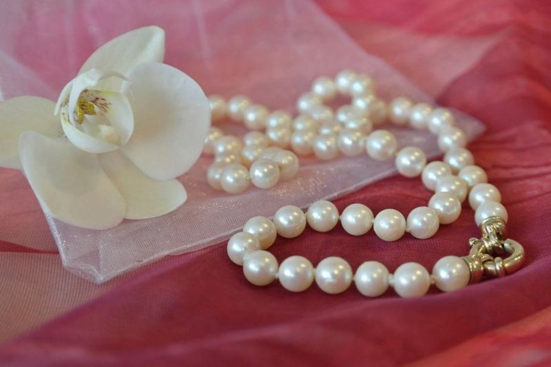 Collar de perlas brillante con cierre dorado junto a una orquídea blanca