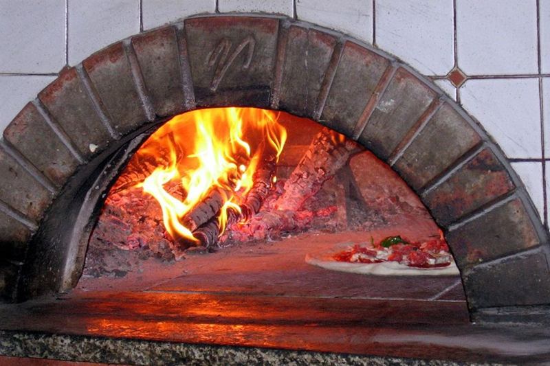 Horno de leña para pizza encendido, con suelo de piedra y bóveda de ladrillo