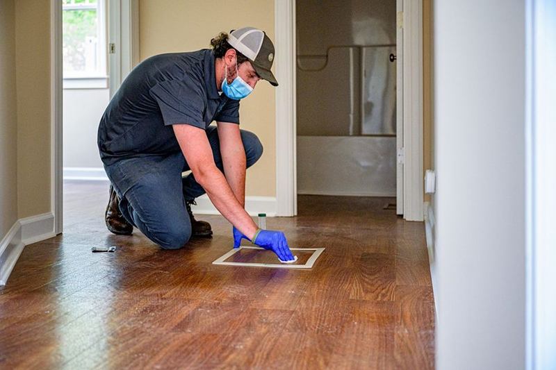 Gloved cleaner wiping the wooden floor of an empty apartment