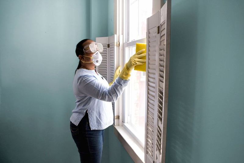 Person wearing goggles, a respirator mask and gloves cleaning a window frame, removing mould from walls safely
