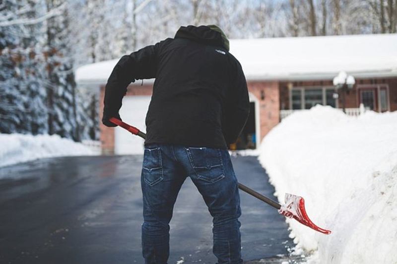 Hombre que retira la nieve del acceso frente a la casa con una pala