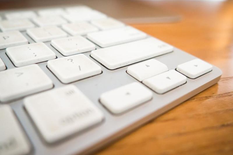 Close-up of a white keyboard on a wooden desk before cleaning