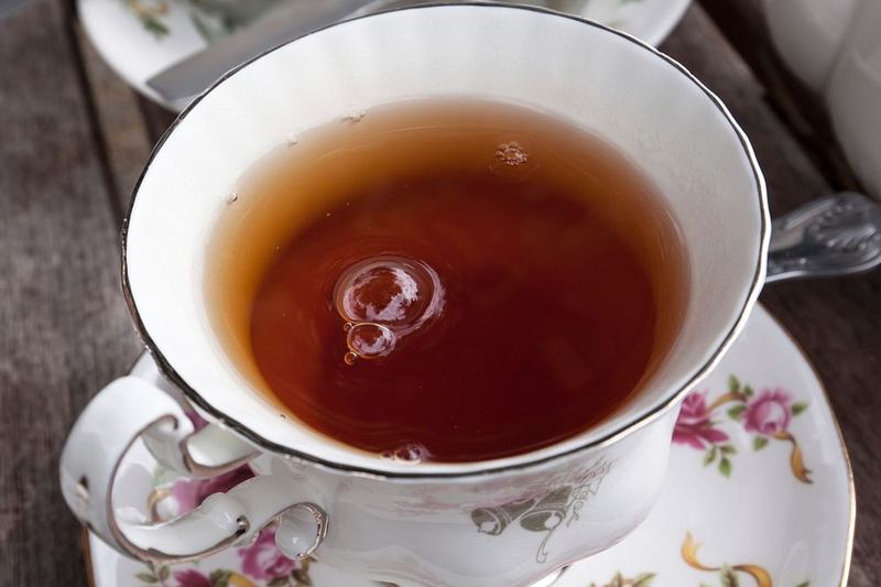 Taza de porcelana con flores llena de té negro, que puede dejar manchas