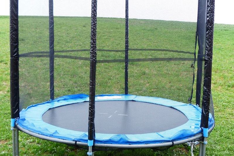 Cama elástica redonda con protector azul y red de seguridad sobre el césped