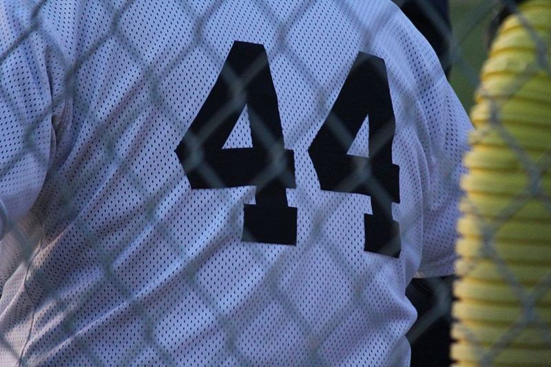 Camiseta blanca de malla con el dorsal 44 negro, tras una valla metálica