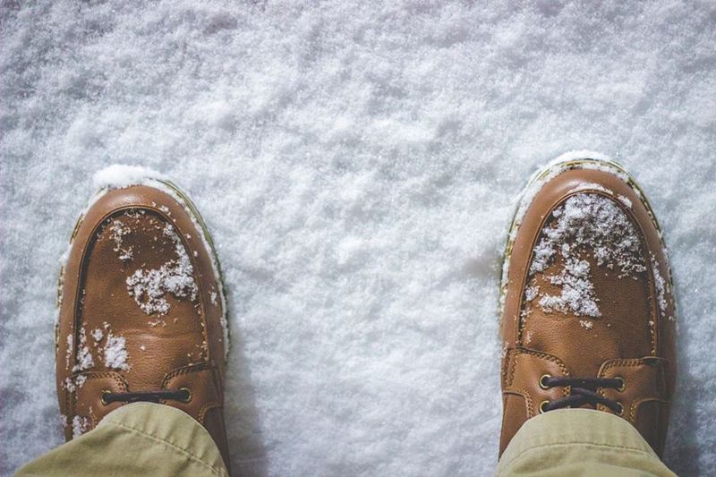 Zapatos de piel marrón con nieve, que hay que proteger de las manchas de agua