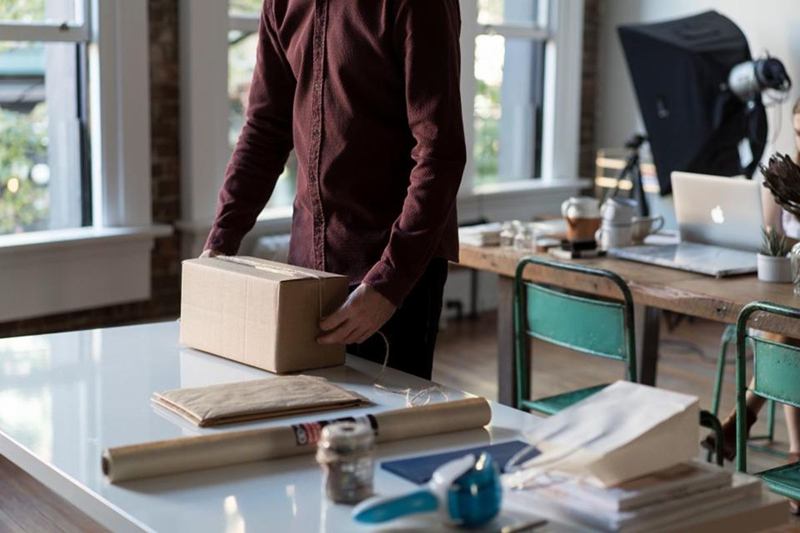 Person packing a moving box at a table, working through a moving checklist