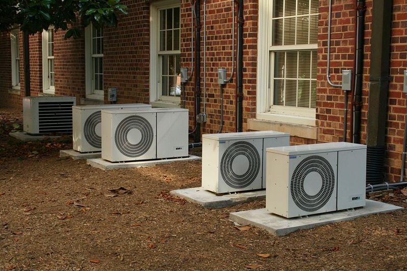 Unidades exteriores con ventilador junto a una fachada de ladrillo, hojas en el suelo