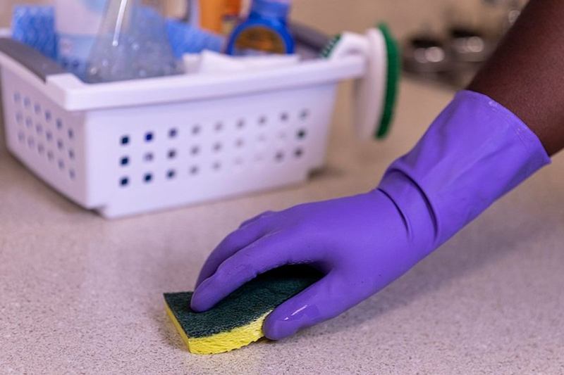 Hand im Gummihandschuh schrubbt Arbeitsfläche – wie viele Stunden braucht die Putzfrau
