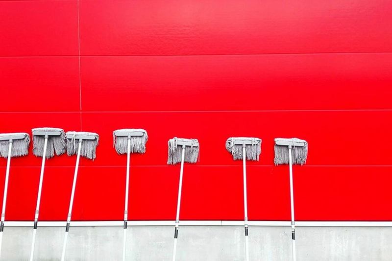 Siete fregonas en fila contra una pared roja: lavar la fregona con regularidad