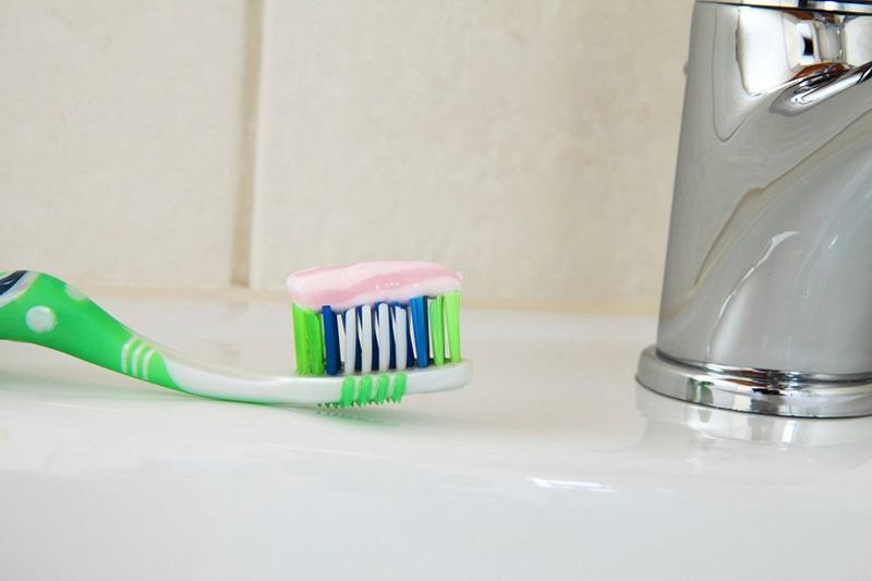 Cepillo con pasta de dientes junto al grifo: limpiar con pasta de dientes